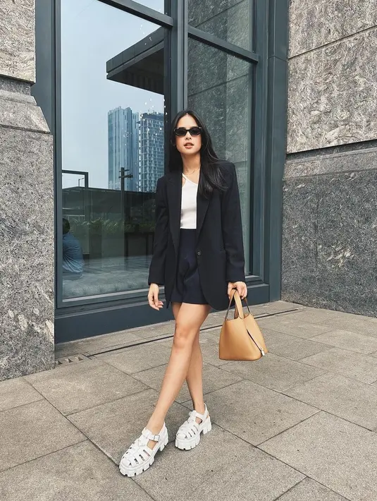Maudy Ayunda mengenakan inner putih yang memadukan blazer dan short skirt hitam.