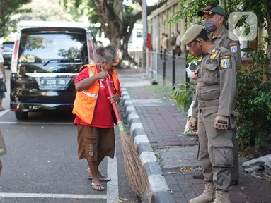Petugas Satpol PP memberikan sanksi menyapu kepada warga yang tidak menggunakan masker di kawasan Pasar Baru, Jakarta, Jumat (21/8/2020). Sanksi tersebut dilakukan sebagai bagian dari upaya pencehagan penyebaran virus covid-19. (Liputan6.com/Immanuel Antonius)