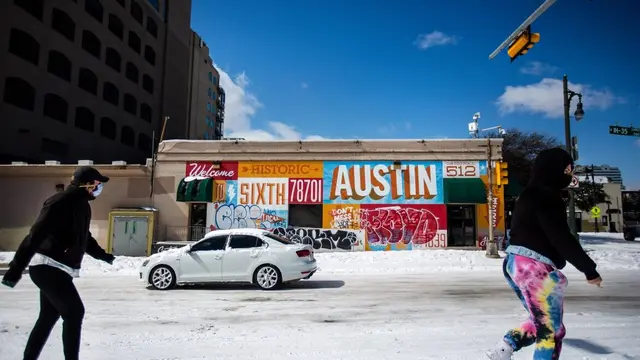 Orang-orang yang berjalan sepanjang jalan yang tertutup salju di Austin, Texas. Badai Musim Dingin Uri telah membawa cuaca dingin bersejarah ke Texas, menyebabkan kemacetan lalu lintas dan pemadaman listrik. [Montinique Monroe / Getty Images / AFP]