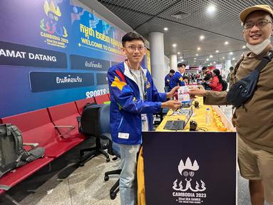 Jurnalis Bola.com, Gregah Nurikhsan (kanan) memegang ID card peliputan SEA Games 2023 Kamboja yang telah diregistrasi oleh petugas di Bandara Internasional Phnom Penh, Kamboja, pada Jumat (28/4/2023). Proses registrasi berupa penempelan hologram untuk kontingen dan wartawan. (Bola.com/Abdul Aziz)