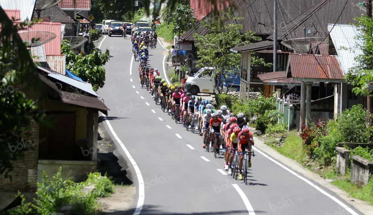 Pebalap melintasi perkampungan sepanjang etape ke-5 Tour de Singkarak dari Pantai Carocok-Painan menuju pantai Gondoriah-Pariaman, Sumatera Barart. (Bola.com/Nicklas Hanoatubun)