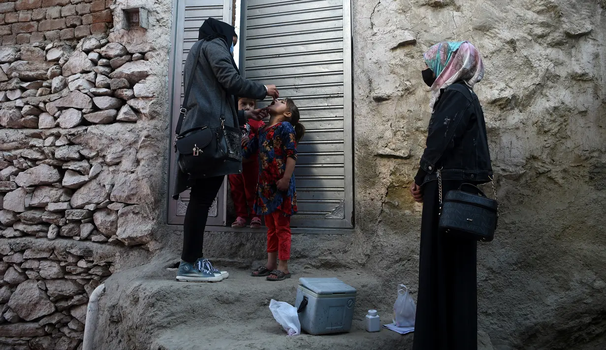 Petugas kesehatan (kiri) memberikan vaksin polio kepada seorang anak selama kampanye vaksinasi di kawasan tua Kabul, Afghanistan pada 8 November 2021. Vaksinasi tersebut merupakan yang pertama sejak Taliban berkuasa di Afghanistan. (WAKIL KOHSAR / AFP)