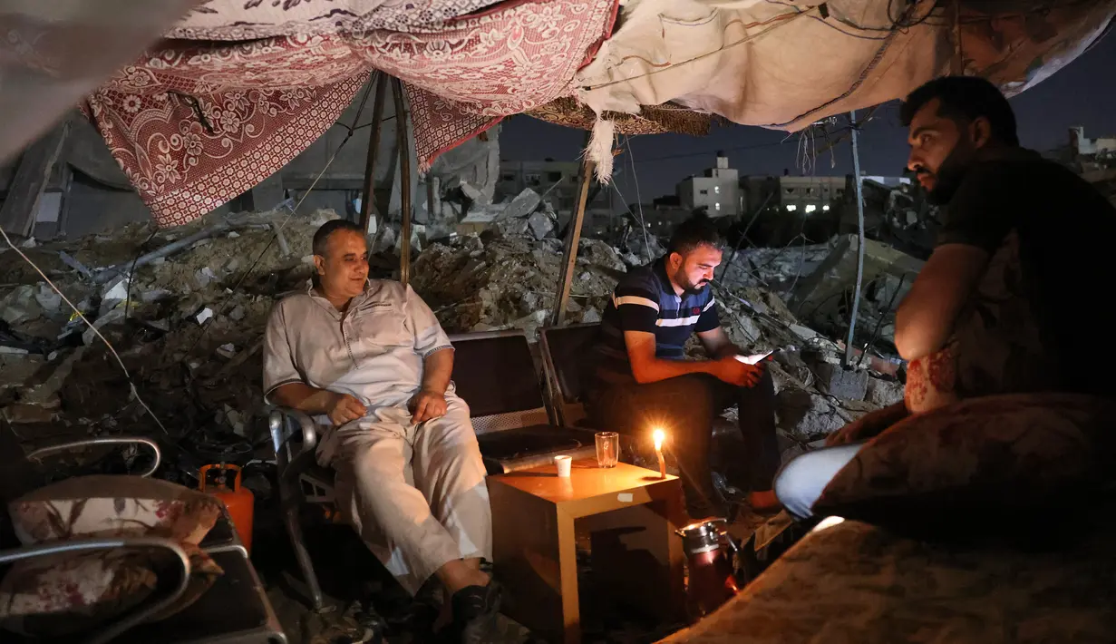 Warga Palestina duduk di tenda yang didirikan di atas reruntuhan bangunan yang hancur dalam serangan udara Israel di Kota Gaza (24/5/2021). Menurut kementerian kesehatan Gaza, perang tersebut menewaskan 248 warga Palestina, termasuk 66 anak-anak, dan melukai lebih dari 1.900 orang. (AFP/Mohamed Abed