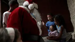 Santa Claus menghibur seorang balita saat mengunjungi kawasan kumuh Petare di Caracas, Venezuela (11/12). Kunjungan Santa Claus ini untuk menghibur anak-anak Petare dalam menyambut datangnya natal. (Reuters/Ueslei Marcelino)