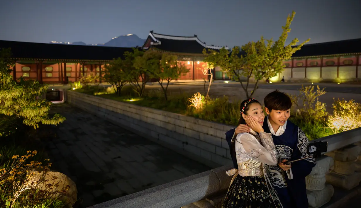 Pengunjung mengenakan gaun tradisional Korea, hanbok sambil berpose saat kunjungan malam ke Istana Gyeongbokgung di Seoul, 4 Oktober 2019. Kunjungan malam tersedia pada minggu ketiga dan keempat setiap bulan mulai dari 26 April sampai 31 Oktober, kecuali pada bulan Agustus. (Photo by Ed JONES / AFP)