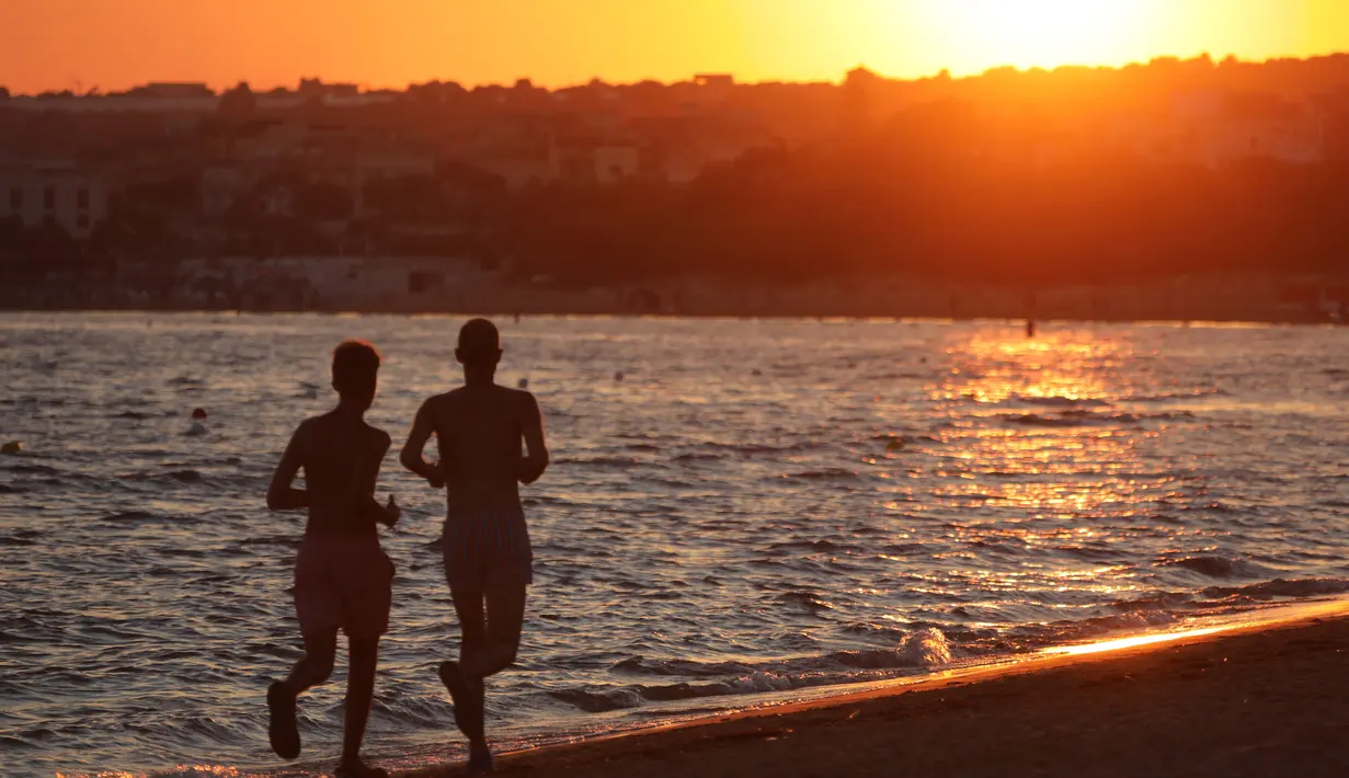 Dua orang berlari saat menikmati matahari terbenam di pantai Sampieri, Sisilia, (31/7). (AFP Photo/Ludovic Marin)