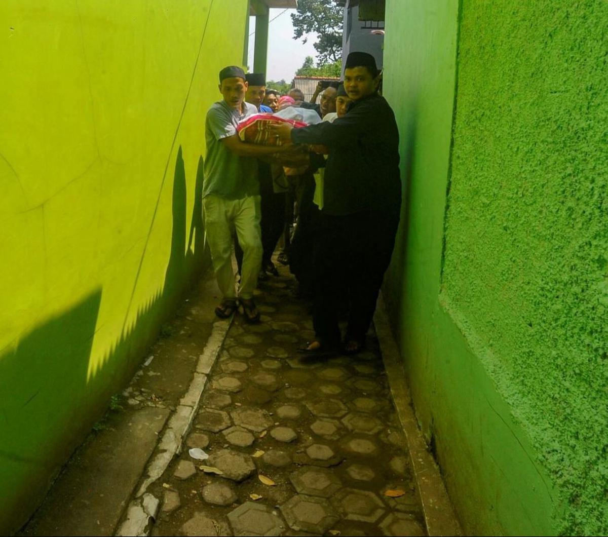 Setelah tiba diantar dengan mobil ambulans, jenazah digotong oleh warga dan keluarga dengan berjalan kaki menuju rumah duka melewati gang sempit di sebuah permukiman padat penduduk di Depok. Foto: merdeka.com / Arie Basuki