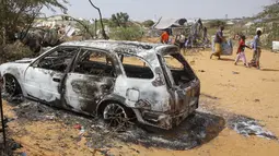 Warga berjalan melewati puing-puing kendaraan yang hancur dalam serangan terhadap polisi dan pos pemeriksaan di pinggiran ibu kota Mogadishu, Somalia (16/2/2022). Serangan oleh kelompok ekstremis al-Shabab pada hari Rabu menewaskan lima orang dan melukai 16 orang. (AP Photo/Farah Abdi Warsameh)