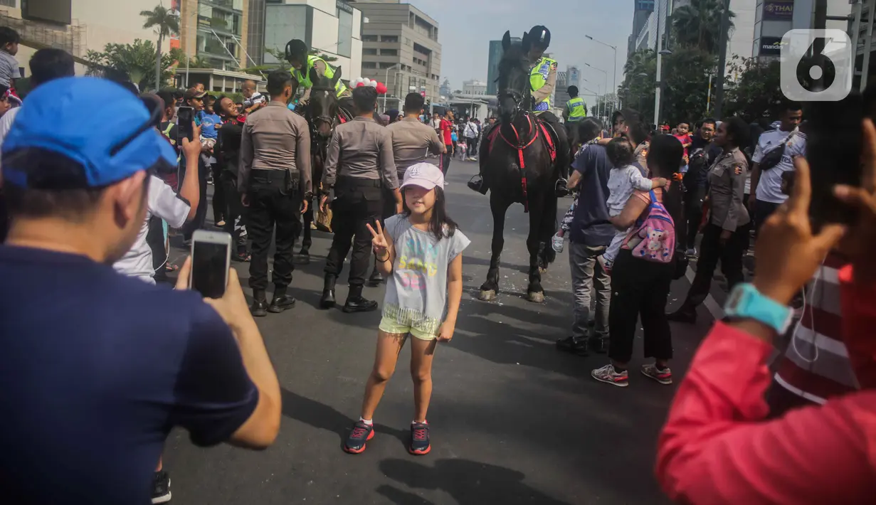 Seorang anak berfoto dengan latar polisi berkuda dari Direktorat Polisi Satwa Mabes Polri yang mengawasi keamanan di kawasan Bundaran HI, Jakarta, Minggu (17/11/2019). Polisi berkuda tersebut khusus ditugaskan mengawasi keamanan CFD serta memperkenalkan kepada warga. (Liputan6.com/Faizal Fanani)