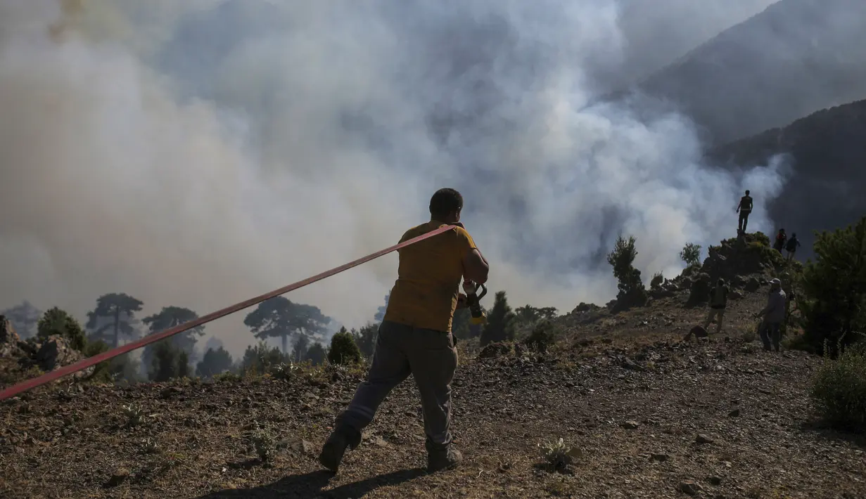 Seorang petugas pemadam kebakaran membawa selang saat memadamkan kebakaran hutan di Koycegiz, Mugla, Turki, Senin (9/8/2021). Kebakaran hutan di Turki telah menewaskan delapan orang serta hewan yang tidak terhitung jumlanya. (AP Photo/Emre Tazegul)