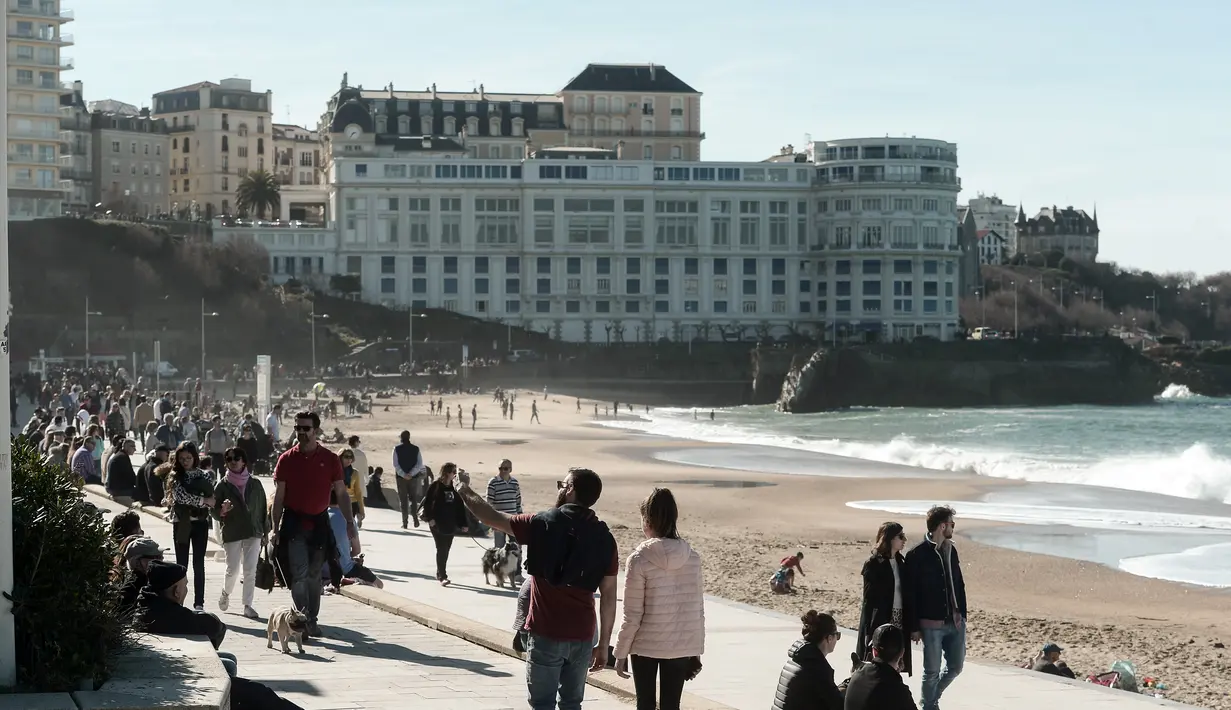 Warga dan turis menikmati cuaca musim dingin yang hangat saat berjalan di sepanjang garis pantai di Biarritz, Perancis (17/2). Pantai Biarritz yang berbatasan dengan Spanyol ini termasuk salah satu wilayah termahal di Prancis. (AFP Photo/Iroz Gaizka)