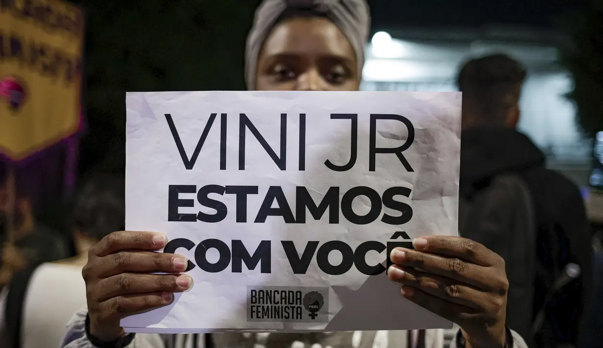 Seorang perempuan memegang tanda dengan pesan yang berbunyi dalam bahasa Portugis; "Vini, kami bersamamu," saat memprotes serangan rasis yang dialami pemain Real Madrid asal Brasil, Vinicius Jr., di luar Konsulat Spanyol di Sao Paulo, Brasil, Selasa (23/5/2023). (AP Photo/Tuane Fernandes)