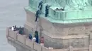 Petugas kepolisian menggunakan tangga membujuk seorang wanita yang memanjat Patung Liberty di New York, Rabu (4/7). Wanita itu terlihat duduk di dekat kaki patung Lady Liberty, sekitar 25 kaki di atas titik pengamatan monumen. (AFP/PIX11 News/Jose ROMERO)