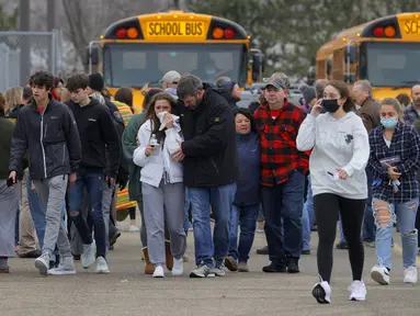 Orang tua berjalan pergi dengan anak-anak mereka dari tempat parkir Meijer, di mana banyak siswa berkumpul menyusul situasi penembak aktif di Oxford High School di Oxford, Michigan (30/11/2021). Polisi telah menahan seorang tersangka penembak. (Eric Seals/Detroit Free Press via AP)