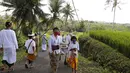 Orang-orang yang memakai masker wajah sebagai pencegahan terhadap wabah virus Corona berjalan ke sebuah pura di sebuah desa di Bali, Senin (21/9/2020). (AP Photo / Firdia Lisnawati)