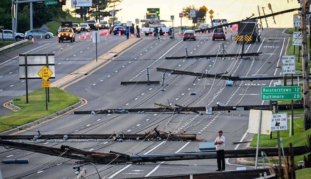 Pemandangan arah timur dari Route 97, seorang pria berdiri melihat tiang listrik yang tumbang di Route 140, Westminster, Maryland, Amerika Serikat, Selasa (8/8/2023). Tiang listrik bertumbangan setelah badai dahsyat melanda area tersebut pada Senin malam. (Jerry Jackson/The Baltimore Sun via AP)