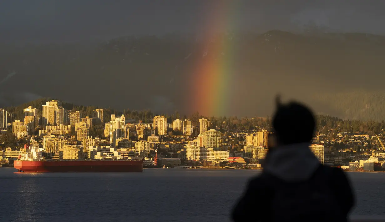 Siluet seorang pria saat mengambil gambar pelangi di pusat kota Vancouver, British Columbia, Kamis (18/3/2021).  Vancouver dikenal di dunia akan keindahannya. Kota ini memiliki salah satu dari taman kota terbesar di Amerika Utara, Stanley Park. (Jonathan Hayward / The Canadian Press via AP)