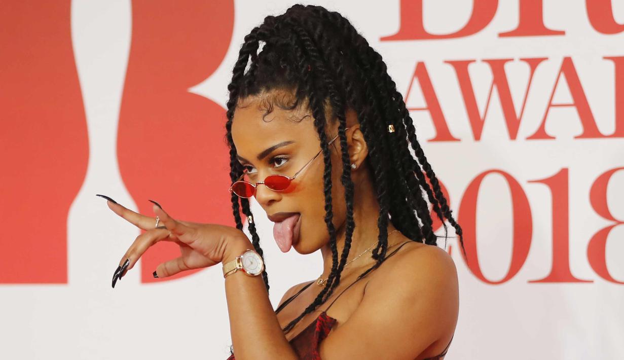 Diana De Brito, yang dikenal sebagai IAMDDB berpose di karpet merah saat tiba menghadiri BRIT Awards 2018 di London, Inggris (21/2). Rapper asal Inggris ini tampil seksi dengan busana transparan sambil membawa mawar berwarna putih. (AFP Photo/Tolga Akmen)