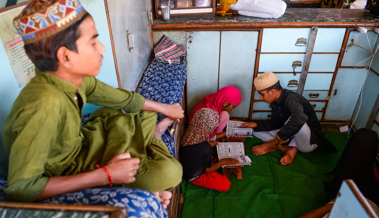 Anak-anak membaca Alquran di sebuah toko yang tutup selama bulan Ramadan saat penerapan lockdown di New Delhi, Senin (4/5/2020). Di emperan toko-toko yang tutup, umat muslim melaksanakan salat jemaah dengan menjaga jarak aman dan beberapa lainnya membaca kitab suci Alquran. (Sajjad HUSSAIN/AFP)