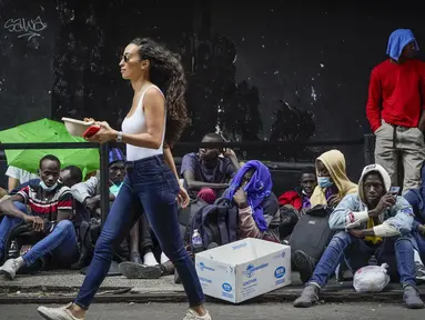 Pejalan kaki melewati para migran yang menunggu dalam antrean di luar The Roosevelt Hotel yang digunakan oleh kota sebagai tempat tinggal sementara, Senin, 31 Juli 2023, di New York. (AP Photo/John Minchillo)