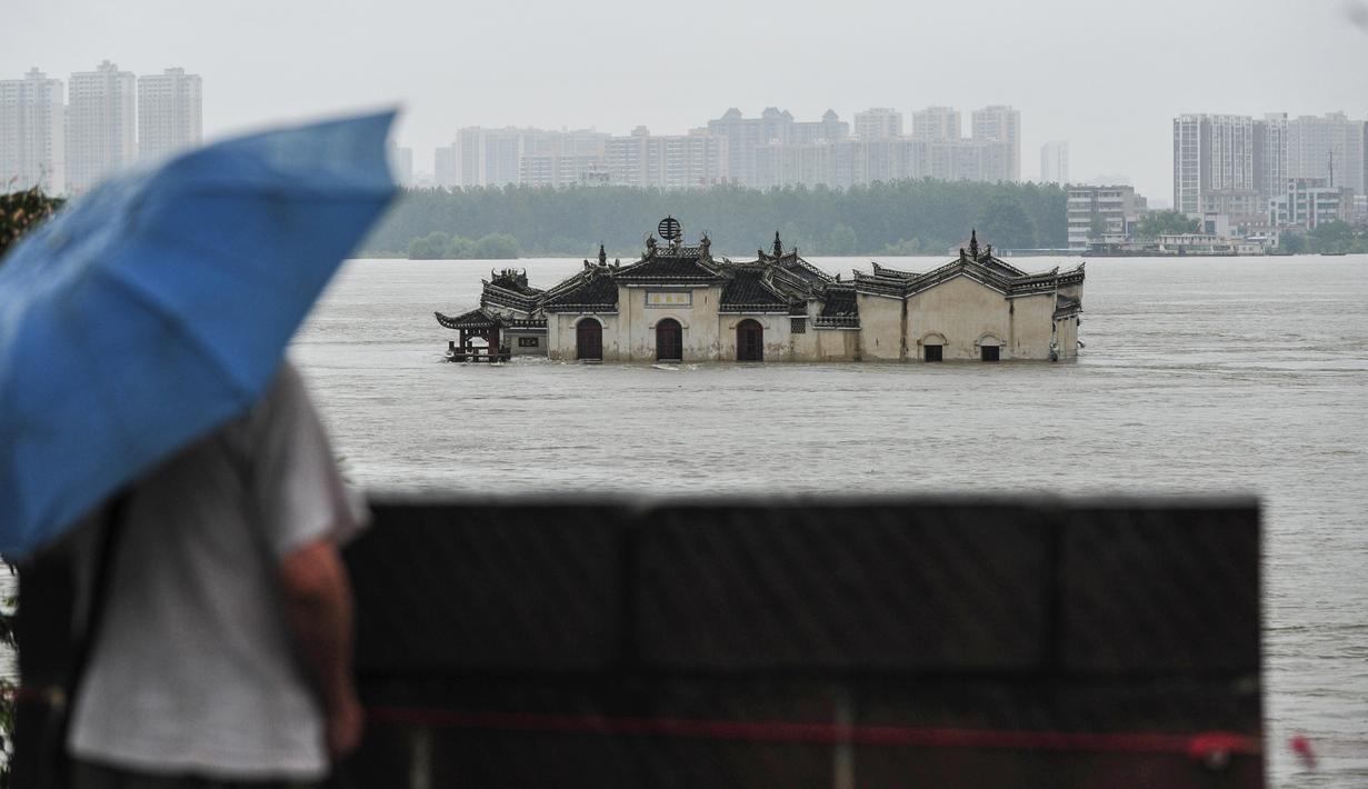 Warga memandangi kuil Guanyinge berumur 700 tahun yang dibangun di atas batu, terendam banjir akibat meluapnya sungai Yangtze di Wuhan, provinsi Hubei pada 19 Juli 2020. Hujan lebat sejak bulan Juni telah menyebabkan sedikitnya 141 orang tewas dan memaksa hampir 15 juta orang dievakuasi. (STR/AFP)