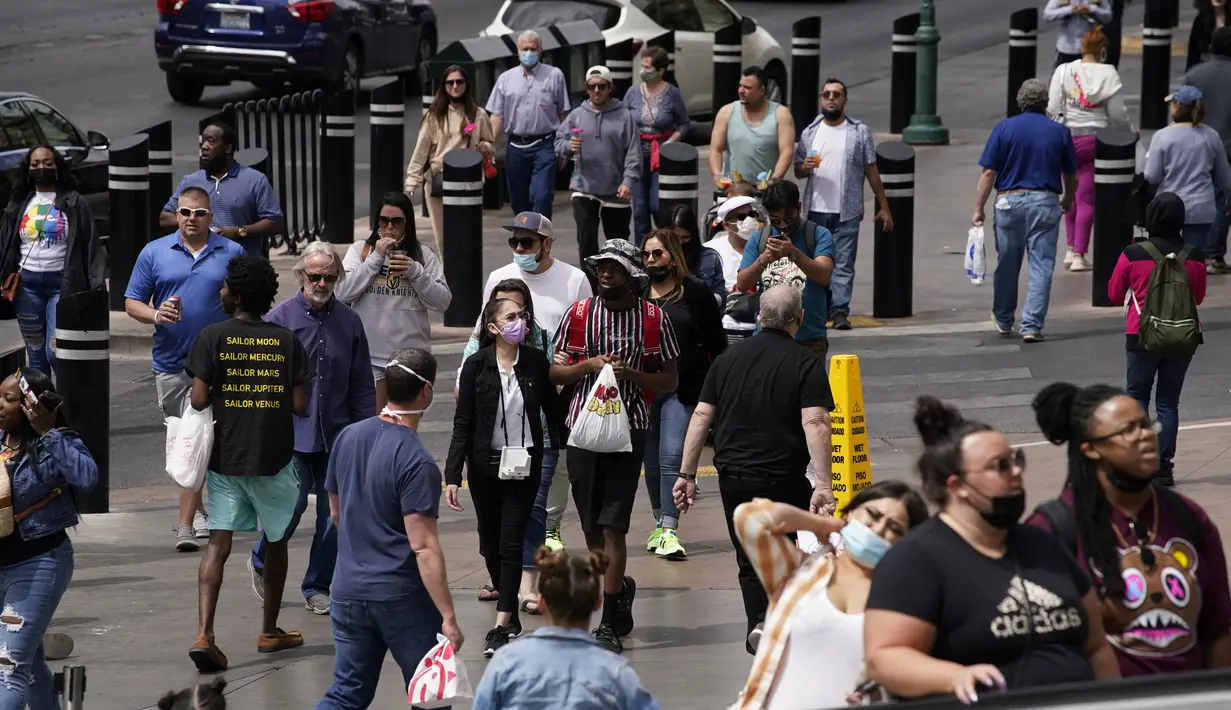 Pejalan kaki dengan masker dan tanpa masker berjalan di sepanjang Las Vegas Strip, di Las Vegas Selasa (27/4/2021). Warga Amerika Serikat (AS) yang telah menerima vaksin COVID-19 tidak lagi diwajibkan mengenakan masker saat berada di luar ruangan jika tidak ada kerumuman. (AP Photo/John Locher)