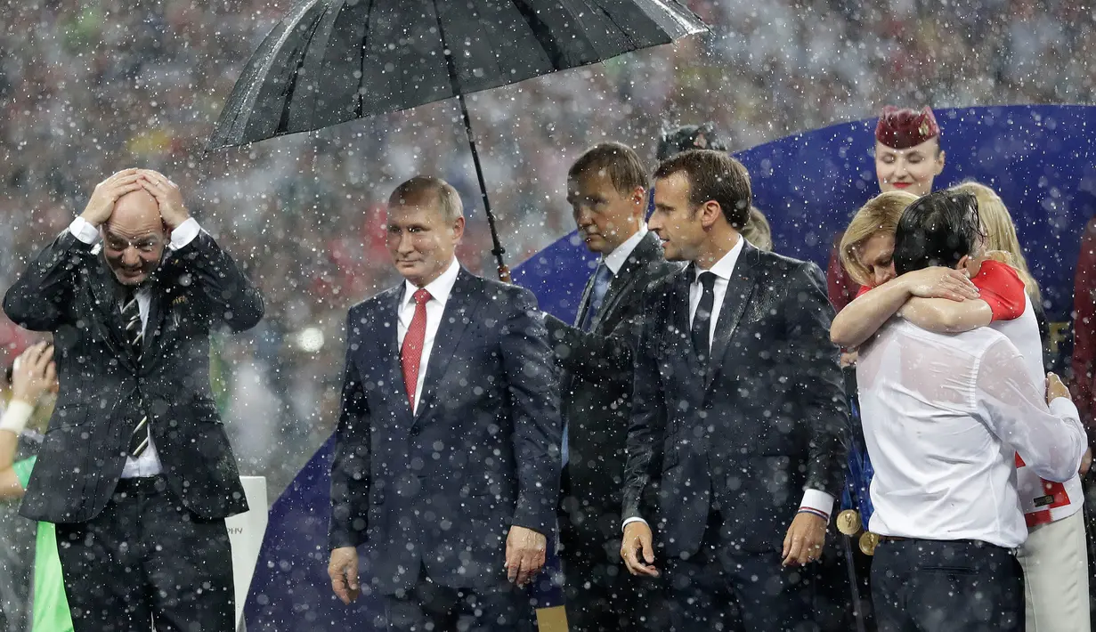 Presiden FIFA Gianni Infantino menutupi kepalanya dengan tangan sementara Presiden Rusia, Vladimir Putin dilindungi payung saat hujan turun selama penyerahan medali dan trofi Piala Dunia 2018 di Stadion Luzhniki, Minggu (15/7). (AP/Matthias Schrader)