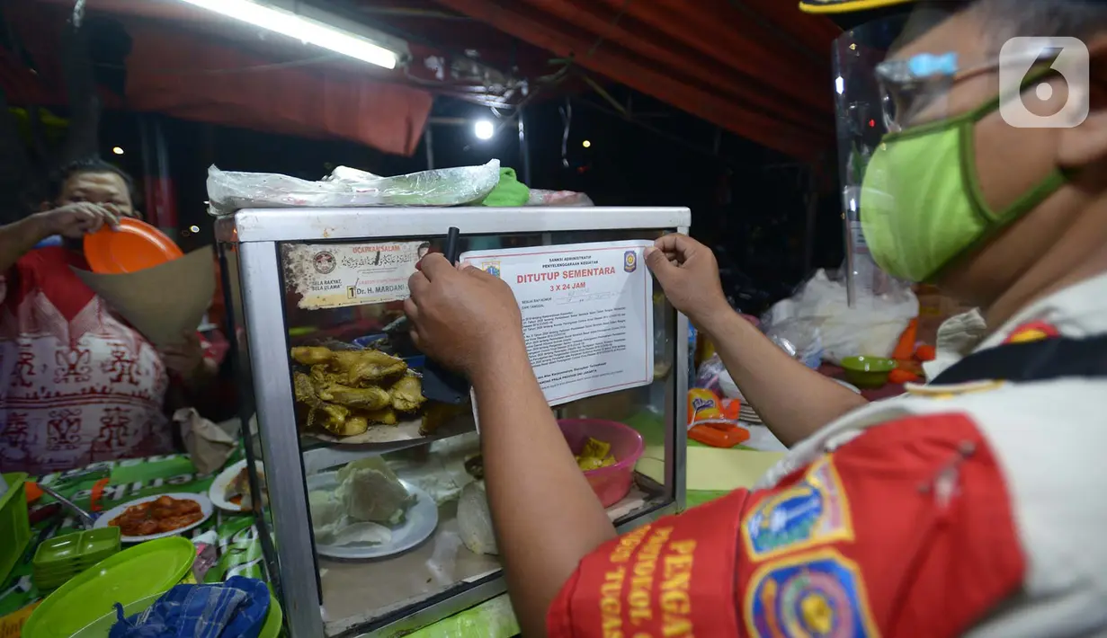 Petugas Satpol PP menempelkan stiker penutupan sementara tempat makan saat penertiban penerapan PSBB di wilayah Kecamatan Pulogadung, Jakarta, Jumat (18/9/2020). Malam, Razia dilakukan memastikan ketidakadaannya konsumen makan ditempat tersebut. (merdeka.com/Imam Buhori)
