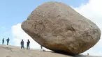 Pengunjung berdiri dekat batu 'Krishna's Butter Ball' yang terkenal di Mahabalipuram, India, Kamis (3/10/2019). Batu yang dikenal masyarakat sekitar dengan nama Vaan Irai Kal ini terletak di lereng dengan kemiringan 45 derajat. (ARUN SANKAR / AFP)