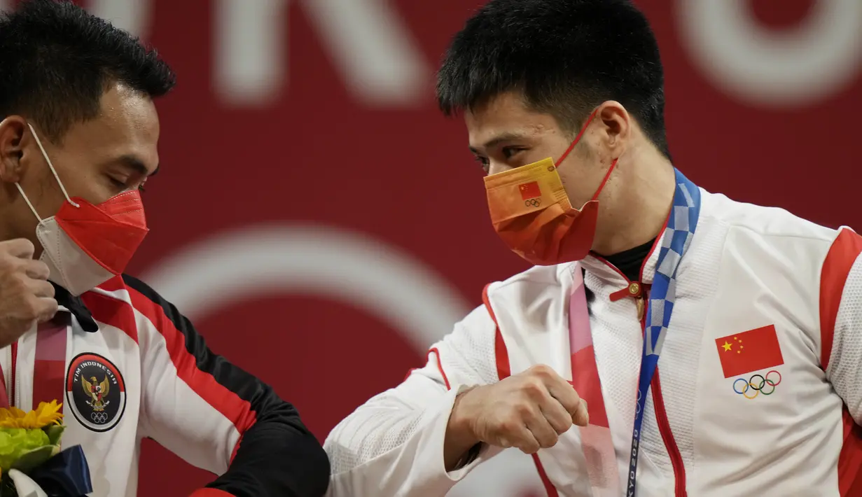 Peraih medali emas Li Fabin dari China (kanan) merayakan di podium dengan peraih medali perak Eko Yuli Irawan dari Indonesia dalam kelas 61kg putra Grup A cabor angkat besi Olimpiade Tokyo 2020 di Tokyo International Forum, Minggu (25/7/2021). (AP Photo/Luca Bruno)