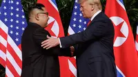 Presiden AS Donald Trump  berjabat tangan dengan Pemimpin Korea Utara, Kim Jong-un dalam pertemuan bersejarah di resor Capella, Pulau Sentosa, Selasa (12/6). Kim dan Trump hadir di depan jurnalis dengan latar belakang bendera Korut dan AS. (AP/Evan Vucci)