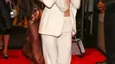 Setelah tampil dramatis dengan gaun couture di red carpet, Lisa beralih ke power dressing yang lebih playful. Ia terlihat meninggalkan hotel dengan setelan cream suit berpotongan tailored dengan low-rise flared pants. Di balik blazer, terselip satin bralette yang memberi sentuhan sensual. Aksesori seperti platform heels dari Stuart Weitzman, trunk bag berkilau, dan perhiasan berlian memperkuat aura glam yang effortless. [@voguehongkong].
