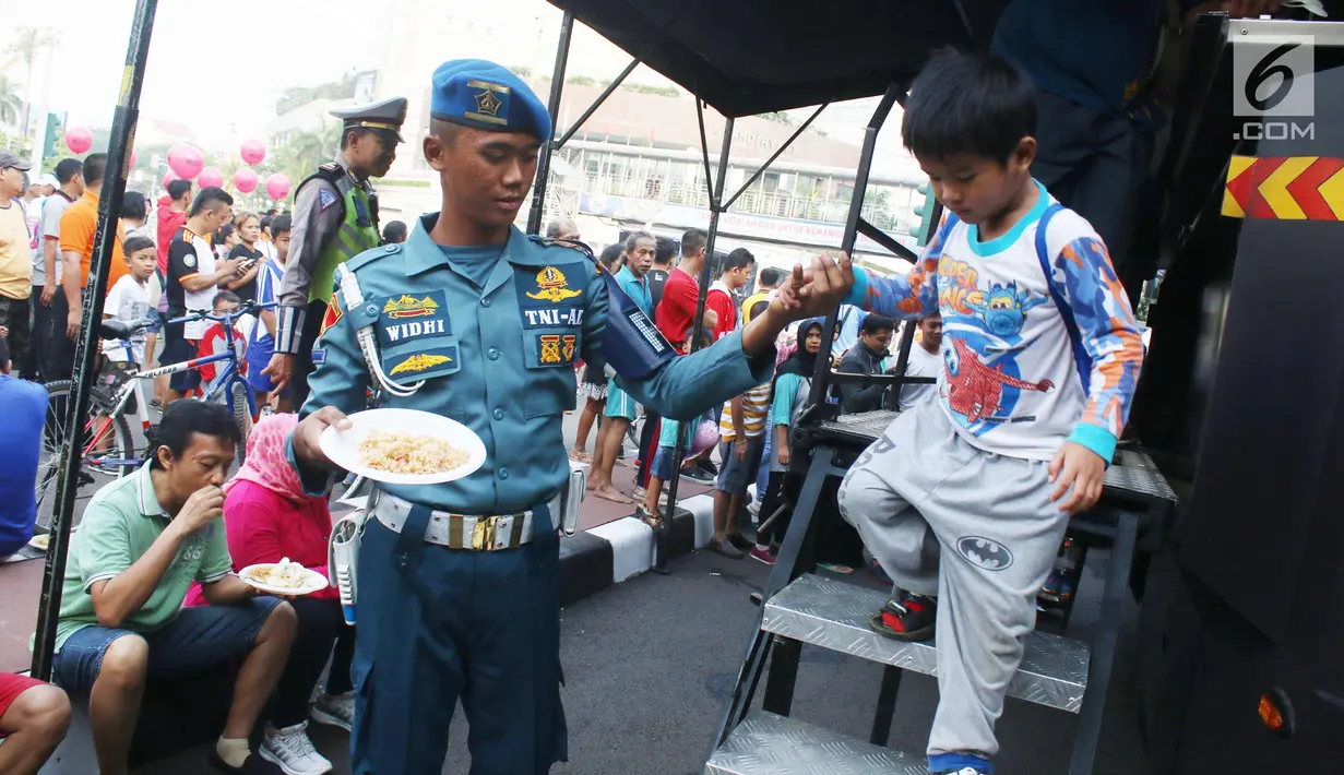 Prajurit Korps Marinir TNI AL membantu seorang anak turun dari truk saat car free day di Jakarta, Minggu (5/11). Kegiatan bagi-bagi nasi goreng ini dalam rangka menyambut HUT Marinir ke-72. (Liputan6.com/Angga Yuniar)