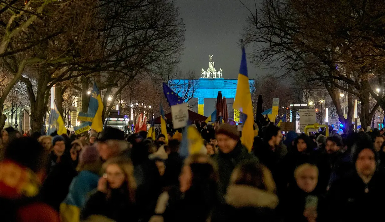 Para pengunjuk rasa tiba di Gerbang Brandenburg, diterangi dengan warna bendera Ukraina, saat demonstrasi untuk menandai peringatan satu tahun invasi besar-besaran Rusia ke Ukraina di Berlin, Jerman, 24 Februari 2023. (AP Photo/Markus Schreiber)