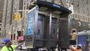 Para pekerja memindahkan bilik telepon umum terakhir NYC di dekat Seventh Avenue dan 50th Street di Midtown Manhattan, New York City, pada 23 Mei 2022. Telepon umum mulai menghilang dari jalan-jalan di New York pada awal 2000-an saat penggunaan telepon selular menyebar, dan kemudian menghilang lebih cepat pada 2010-an saat terjadi booming telepon pintar. (TIMOTHY A. CLARY / AFP)