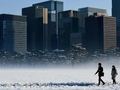 Warga melintasi jalan yang tertutup salju  di dekat Istana Kekaisaran di Tokyo, Jepang (23/1). Badan cuaca Jepang mengeluarkan peringatan salju pertamanya di kota tersebut setelah empat tahun terakhir. (AFP Photo/Toshifumi Kitamura)