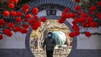 Seorang pria yang mengenakan masker berjalan melewati pepohonan yang dihiasi lentera untuk Tahun Baru Imlek di sebuah taman umum di Beijing, Jumat, 20 Januari 2023. Tahun Kelinci secara resmi dimulai pada 22 Januari. (AP Photo/Mark Schiefelbein)