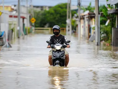 Seorang pria mengendarai sepeda motornya menerjang banjir di Batu Berendam, Malaka, Malaysia, 3 Januari 2022. Banjir besar masih terus menerjang negeri jiran Malaysia. (NAZRULHAD HASHIM/AFP)