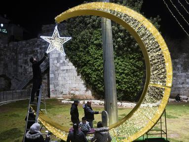 Seorang pria Palestina menggantungkan lampu hias untuk menyambut bulan suci Ramadhan, tepat di luar Kota Tua Yerusalem, Selasa, 21 Maret 2023. (AP Photo/Mahmoud Illean)