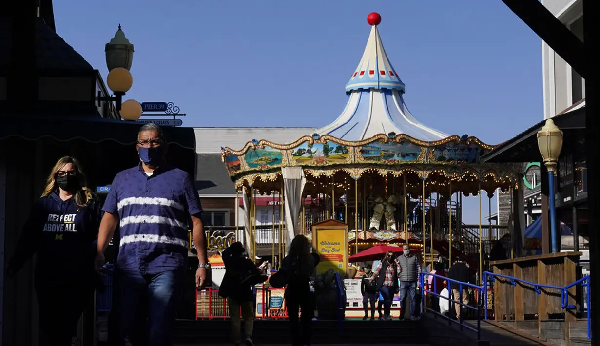 Orang-orang memakai masker saat berjalan di depan komidi putar di Pier 39 saat wabah COVID-19 di San Francisco, California, Amerika Serikat, Kamis (12/11/2020). California menjadi negara bagian kedua selain Texas yang mencatat 1 juta kasus infeksi COVID-19. (AP Photo/Jeff Chiu)