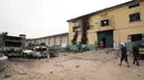 Orang-orang berjalan melewati kendaraan yang terbakar di depan sebuah fasilitas pemasyarakatan seusai serangan oleh kelompok bersenjata di Owerri, Nigeria, Senin (5/4/2021). Enam tahanan dilaporkan telah kembali, dan 35 tahanan lainnya menolak untuk melarikan diri. (AP Photo/David Dosunmu)