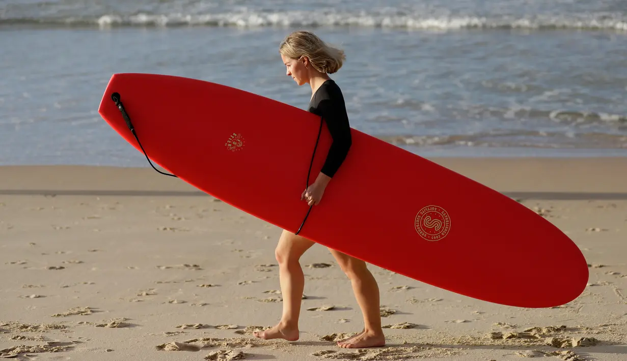 Seorang wanita membawa papan selancar bersiap bermain saat pembatasan sosial Covid-19 mulai dilonggarkan di Pantai Bondi di Sydney, Selasa, (28/4/2020).  Pantai ini terbuka untuk perenang dan peselancar untuk berolahraga saja. (AP Photo/Rick Rycroft)