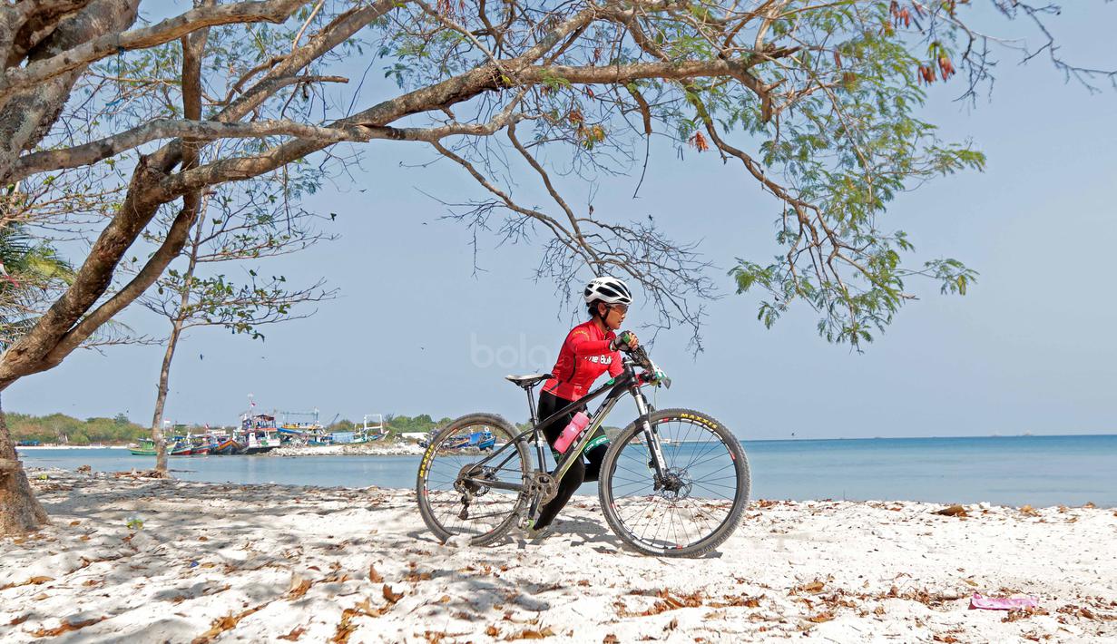 Seorang pebalap wanita Mountain Bike Cross Country Marathon mendorong sepedanya saat melintasi pasir pada Festival Pesona Tanjung Lesung 2017 di Tanjung Lesung, Banten (23/9/2017). MTB XCM tersebut menempuh jarak 48 km. (Bola.com/Nicklas Hanoatubun)
