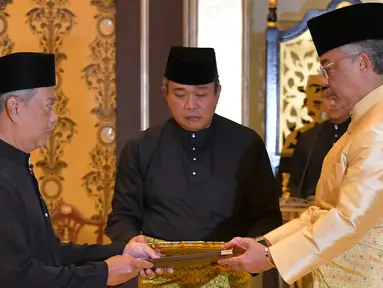 Muhyiddin Yassin (kiri) menerima dokumen dari Raja Sultan Abdullah Sultan Ahmad Shah (kanan) sebelum disumpah sebagai Perdana Menteri Malaysia di Istana Negara, Kuala Lumpur, Minggu (1/3/2020). Muhyiddin Yassin resmi menjadi PM Malaysia. (MASZUANDI ADNAN/MALAYSIA'S DEPARTMENT OF INFORMATION/AFP)