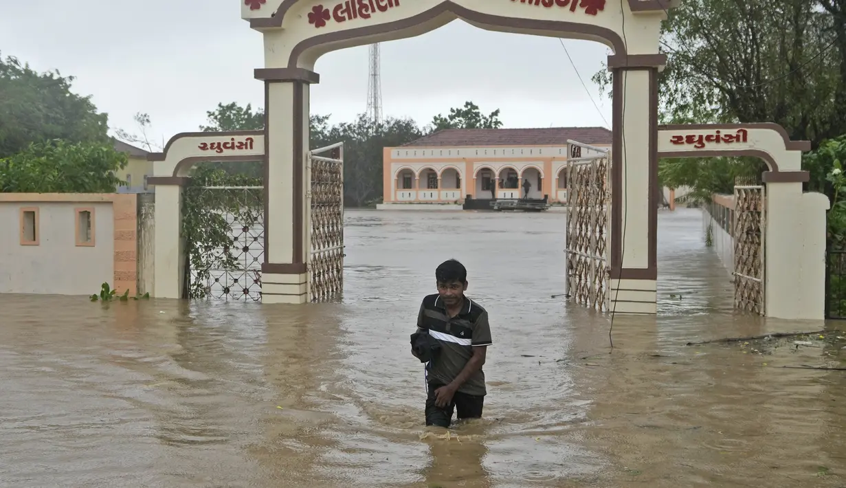 Seorang pria mengarungi jalan yang terendam banjir menyusul angin kencang dan hujan deras setelah topan Biparjoy mendarat di Mandvi di distrik Kutch, negara bagian Gujarat, India Barat, Jumat, 16 Juni 2023. (AP Photo/Ajit Solanki)