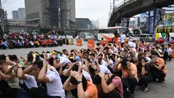Karyawan pusat perbelanjaan menutupi kepala mereka di sepanjang jalan ketika mereka berpartisipasi dalam latihan gempa di Manila (14/11/2019). Latihan ini sebagai bagian dari kesiapsiagaan nasional menyusul berbagai gempa yang melanda pulau Mindanao bulan lalu. (AFP Photo/Ted Aljibe)