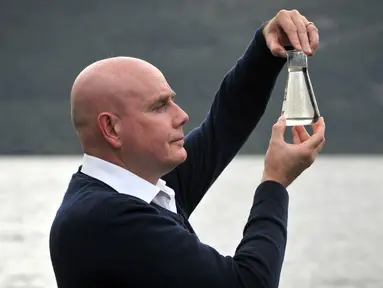 Ahli genetika Universitas Otago Profesor Neil Gemmell berpose dengan wadah air di perairan Loch Ness, Drumnadrochit, Skotlandia, Kamis (5/9/2019). Para ilmuwan mencoba mengurai keberadaan monster legendaris asal Inggris, Loch Ness. (Andy Buchanan/AFP)