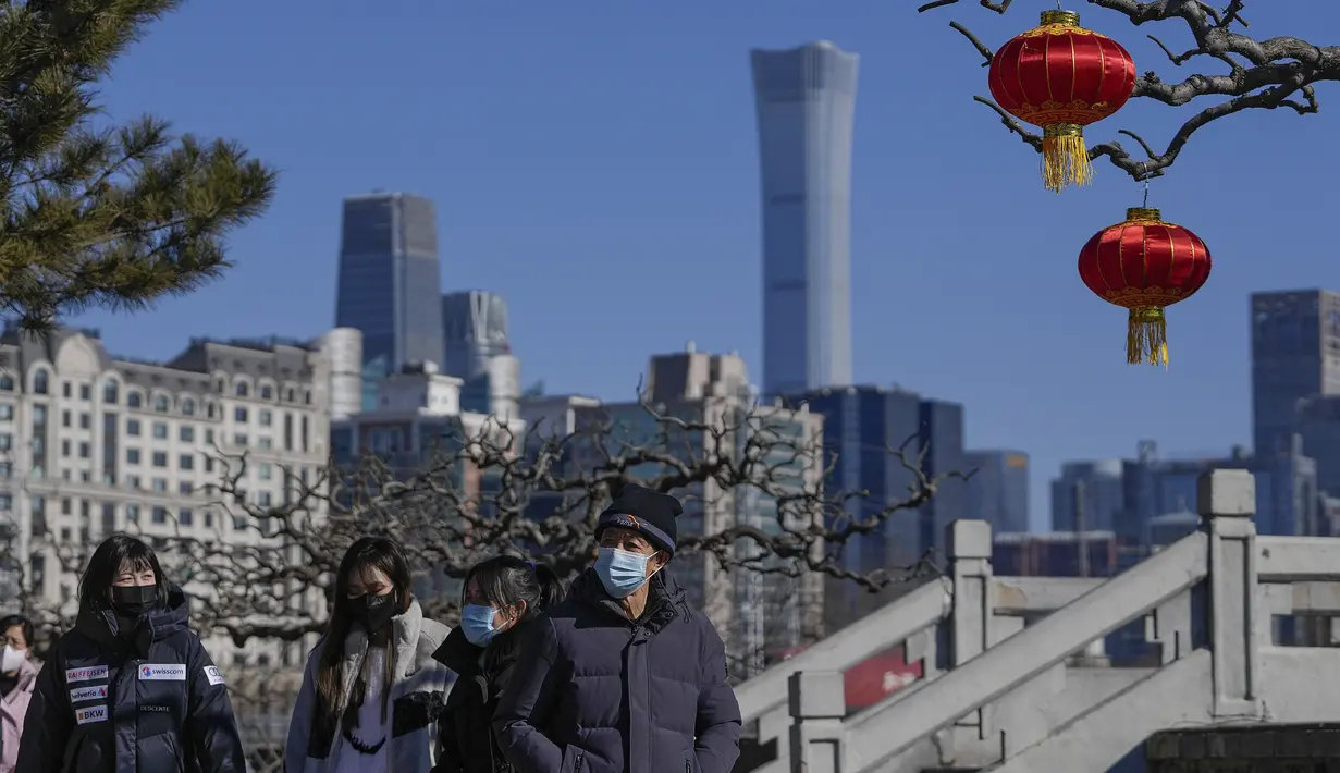 Orang-orang yang memakai masker untuk membantu melindungi dari virus corona berjalan dengan dekorasi lentera jelang Tahun Baru Imlek di sebuah taman di dekat cakrawala kota di Beijing, Kamis (27/1/2022). (AP Photo/Andy Wong)