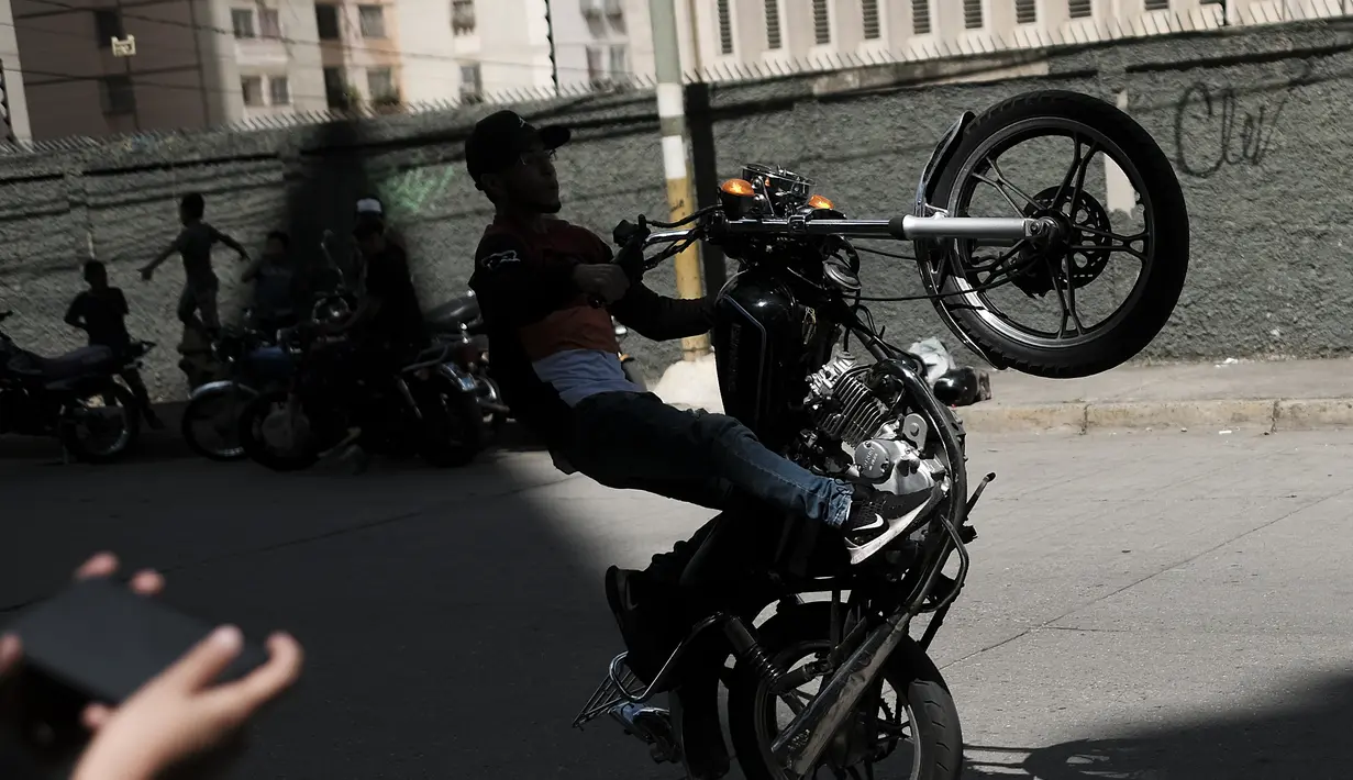 Seorang pengendara sepeda motor melakukan wheelie pada sepeda motornya selama pameran di lingkungan El Valle Caracas, Venezuela, Sabtu (31/7/2021). (AP Photo/Ariana Cubillos)