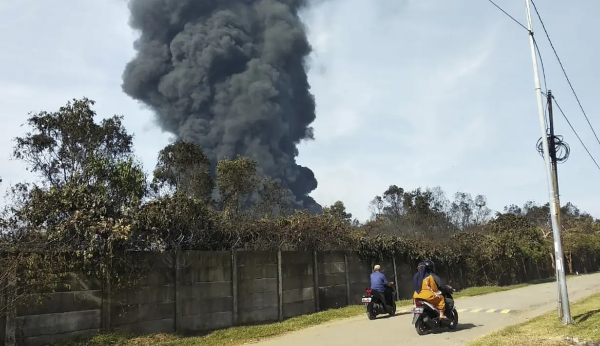 Pengendara motor melewati kepulan asap tebal dari kebakaran yang melanda Kilang Pertamina Balongan di Indramayu, Jawa Barat, Indonesia, Senin (29/3/2021). Tangki T-301G Kilang Balongan milik Pertamina terbakar pada 29 Maret 2021 mulai sekitar pukul 00.45 dini hari. (AP Photo)